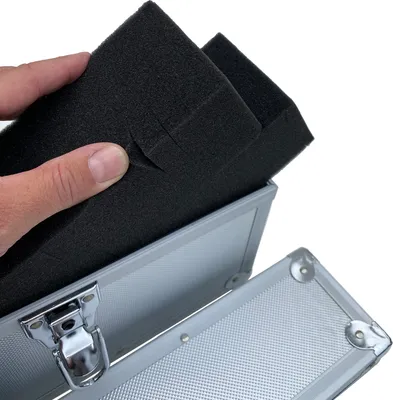 A hand is placing black foam padding into an open silver aluminum case.
