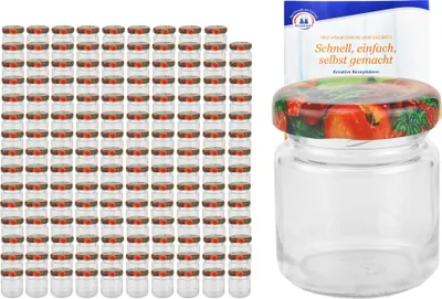 A large stack of small glass jars with fruit-patterned lids, and one jar with a recipe booklet in the background.
