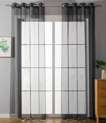 A window with sheer black curtains hanging in front of it, with a grid pattern on the curtains. A small framed picture is on the left, and a wooden dresser with a plant on top is on the right.