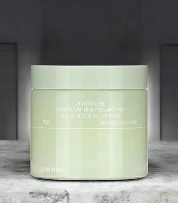 A light green jar of skincare pads sits on a textured surface with a blurred background.