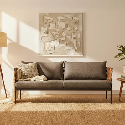 A modern outdoor lounge sofa with cushions, placed on a jute rug in a well-lit room with artwork on the wall.