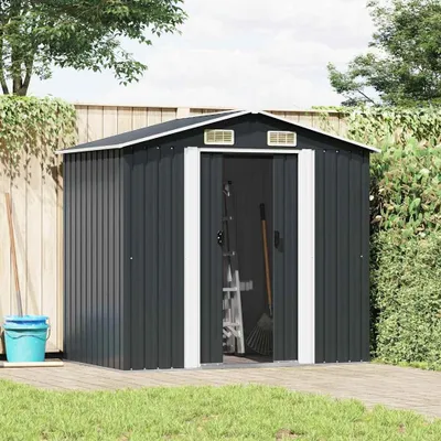 A dark gray metal garden shed with its doors open, showing gardening tools inside. It is situated on a wooden deck with grass in the foreground and a wooden fence and trees in the background.