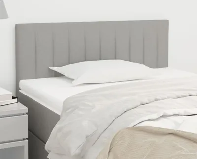 A close-up view of a light gray fabric headboard for a bed, with a white pillow and bedding.