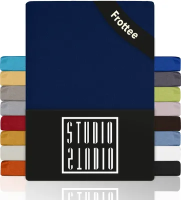 A product image showcasing a navy blue fitted sheet with a black band at the top corner that says 'Frottee'. To the left and right of the main sheet are stacks of fitted sheets in various colors.