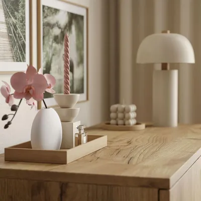 A close-up view of decorative items on a wooden dresser, including a vase with an orchid, candles, and a lamp in the background.