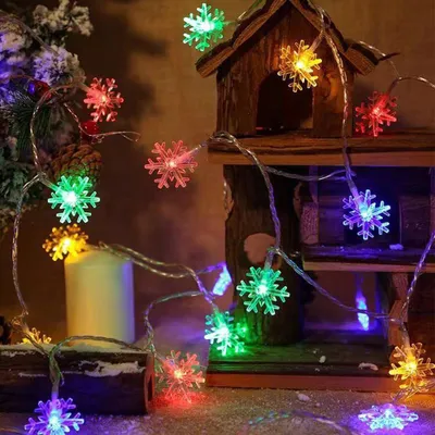 Christmas lights shaped like snowflakes are displayed around a small wooden house decoration, a candle, and a Christmas tree.