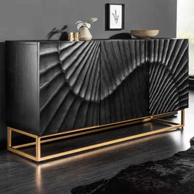 A black wooden sideboard with intricate carvings and a gold metal base, placed in a modern living room setting.