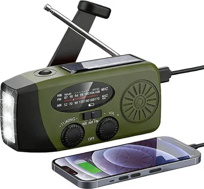 A green emergency radio with a solar panel and LED flashlight is shown, with a smartphone connected to it for charging.
