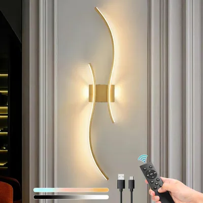 A hand holding a remote control is shown in the foreground, with a modern LED wall lamp mounted on a wall in the background. The lamp has a curved, wave-like design and emits a warm light. There are also USB cables and a color temperature slider graphic vi