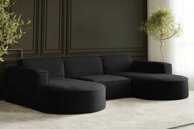 A modern black sectional sofa in a room with dark paneled walls and a potted plant.