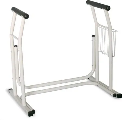 A white metal frame designed to assist with standing up from a toilet, with black grips on the top handles and a small wire basket attached to one side.