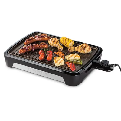 An electric grill with various foods cooking on it.