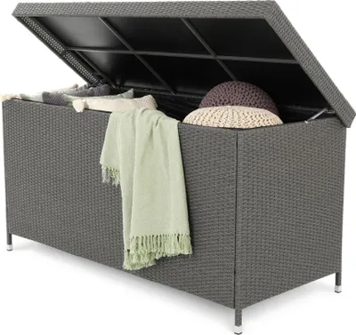 An open grey wicker storage box filled with cushions and blankets.