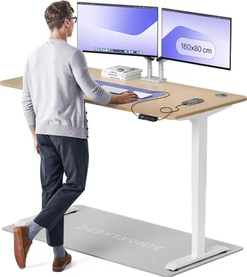 A man is standing at a height-adjustable desk with two monitors, demonstrating its use.