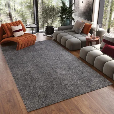 A modern living room with a grey sectional sofa, an orange accent chair, and a large grey rug.