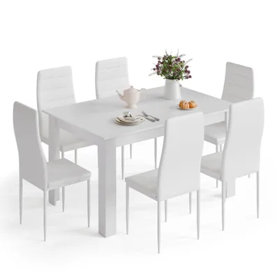 A white dining table with six white chairs, set with a teapot and plates.