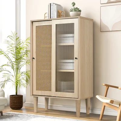 A light wood cabinet with a rattan door and a glass door, filled with white boxes, is placed in a room with a plant and a chair.