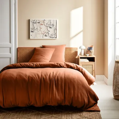 A bedroom scene with a bed dressed in terracotta-colored bedding.