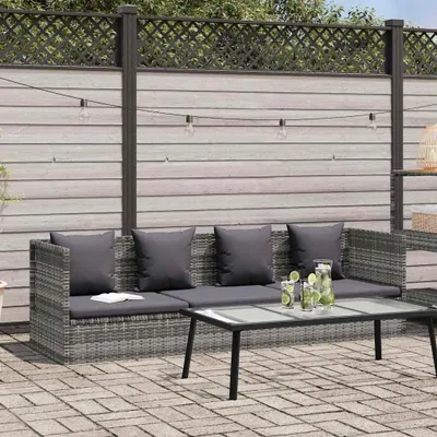 An outdoor sofa set with a coffee table on a paved patio, with a wooden fence and string lights in the background.
