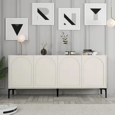 A cream-colored sideboard with arched doors is displayed against a light gray paneled wall. Several framed abstract art pieces are hung on the wall above the sideboard, and decorative items like vases and books are placed on top of it. A robot vacuum clean