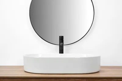 A white oval countertop sink with a black faucet is shown in a bathroom setting.