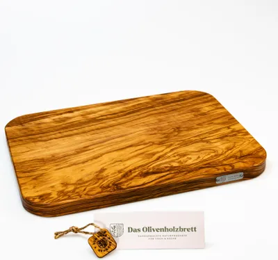 A rectangular olive wood cutting board with rounded corners is displayed on a white background, with a small tag and card in front of it.