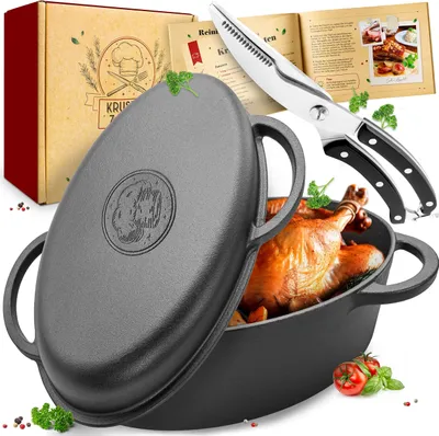 A cast iron Dutch oven with a roasted chicken inside, along with a recipe book and kitchen shears, presented on a white background.