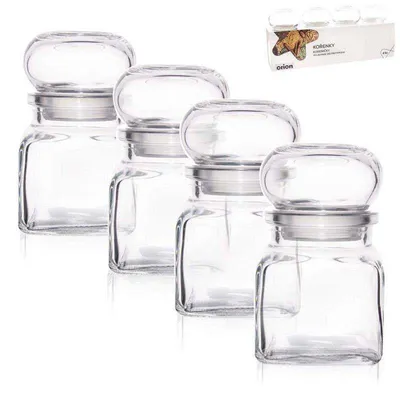 Four clear glass spice jars with silver lids are arranged in a row against a white background. A small box with product information is visible in the upper right corner.