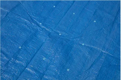 A close-up, textured view of a blue tarp with small white dots scattered across its surface.