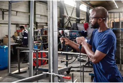 A man is using a Bosch drill in a workshop setting.