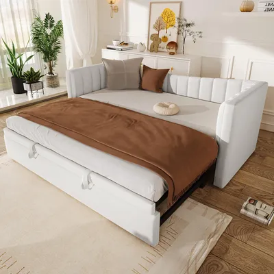 A white daybed with a brown blanket and pillows, set up in a bright room with plants and decor.