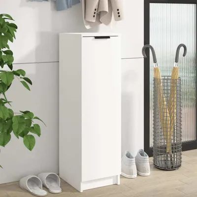 A white shoe cabinet with a black handle is shown in a hallway next to a plant and an umbrella stand. Two pairs of slippers and two pairs of sneakers are on the floor.