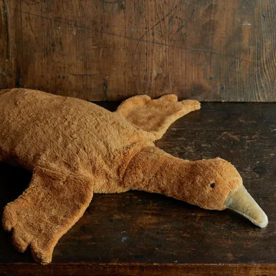 A plush toy goose lies on a wooden surface.