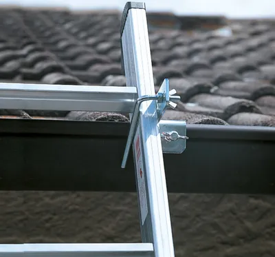 A close-up view of a ladder accessory attached to a gutter on a tiled roof.