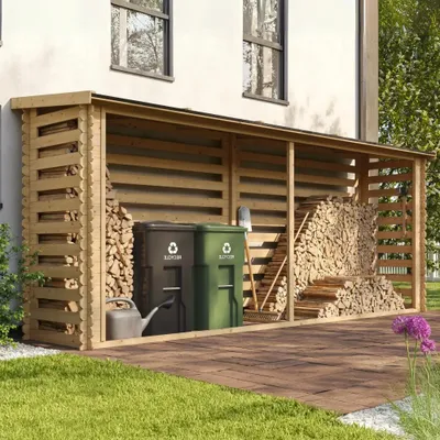A wooden log store filled with firewood, next to two recycling bins and a watering can, situated on a paved patio area next to a house.
