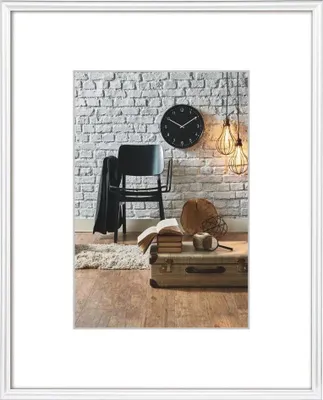 A framed picture of a room with a chair, clock, and suitcase.
