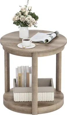 A round, two-tiered coffee table with a rustic wood finish, decorated with a vase of flowers, a cup of coffee, and a newspaper on the top surface, and books and a basket on the lower shelf.