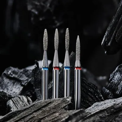 Four diamond burrs are arranged in a row on a dark, rocky surface.