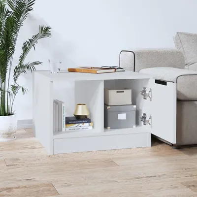 A white coffee table with open compartments on a light wood floor, next to a sofa and a potted plant.
