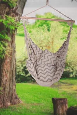 A hammock chair with pillows hanging from a tree in a garden.