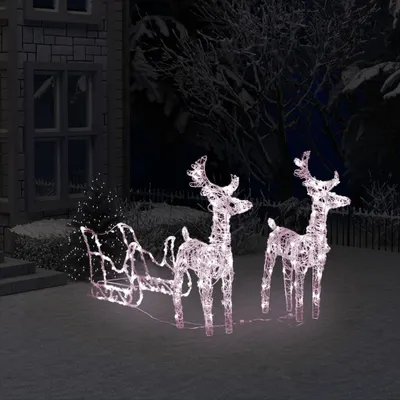 Christmas decoration of illuminated reindeer and sleigh in a snowy yard at night.