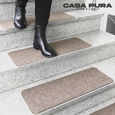 A person wearing black boots walks down a staircase with beige stair mats.