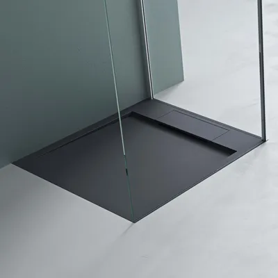 A close-up view of a modern, minimalist shower tray with glass shower walls.