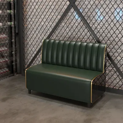 A green sofa with gold trim sits in front of a textured wall and a metal grate.