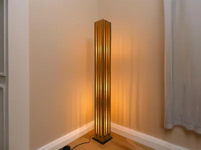 A tall, slender floor lamp with a slatted design stands in the corner of a room, casting a warm glow on the beige walls.