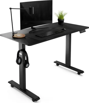 A black standing desk with a monitor, keyboard, mouse, lamp, and headphones.