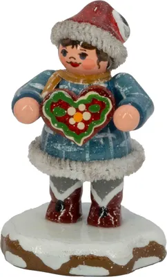 Ein fröhliches Winterkind in blauer Kleidung und roter Mütze hält ein bunt verziertes Lebkuchenherz in den Händen und steht auf einer schneebedeckten Basis