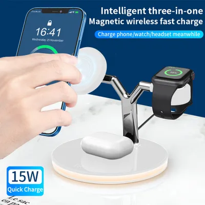 A hand is placing a smartphone onto a white wireless charging stand that also supports an Apple Watch and AirPods.