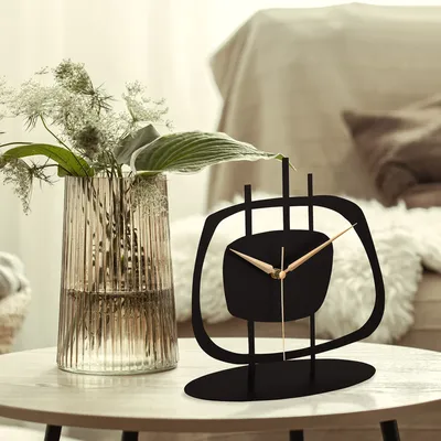 A decorative clock sits on a table next to a vase of flowers.