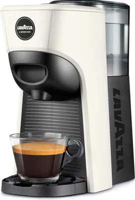 A white and black Lavazza capsule coffee machine with a glass cup of espresso in front of it.